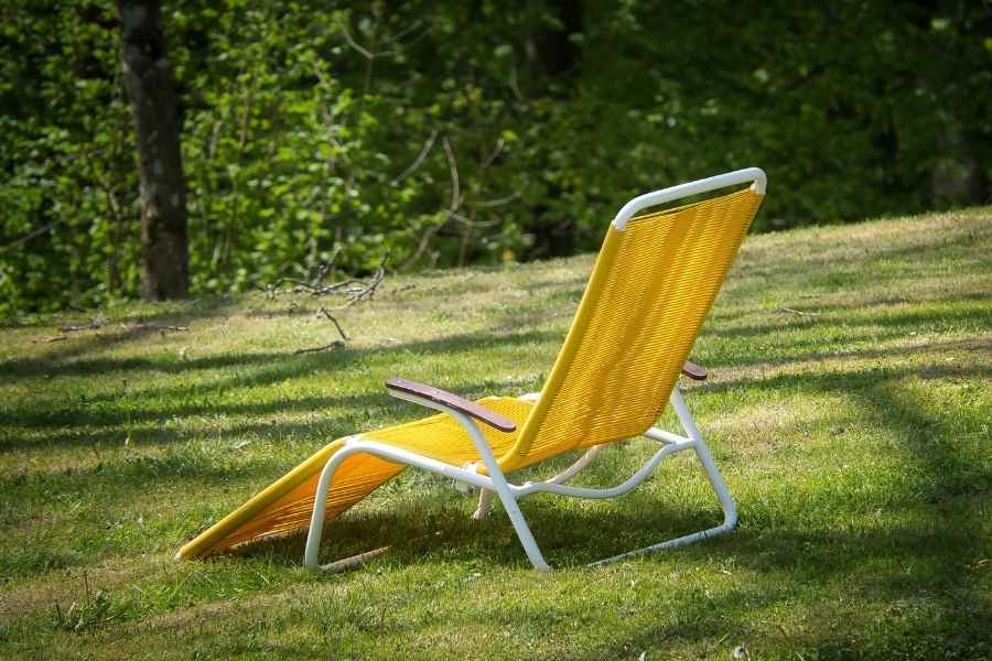 Une chaise longue jaune vif est installée sur une pelouse verdoyante au sein d'un coin détente ombragé.