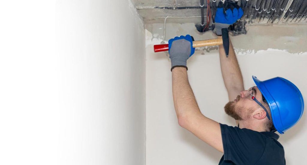 Un ouvrier en bâtiment équipé d'un casque effectue des fixations au plafond, une intervention indispensable avant d'établir le plan plomberie salle de bain douche italienne.