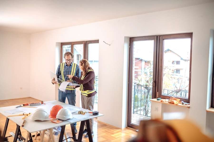 Un homme et une femme en gilets de sécurité discutent de plans sur une table de travail lors de la rénovation de son appartement.
