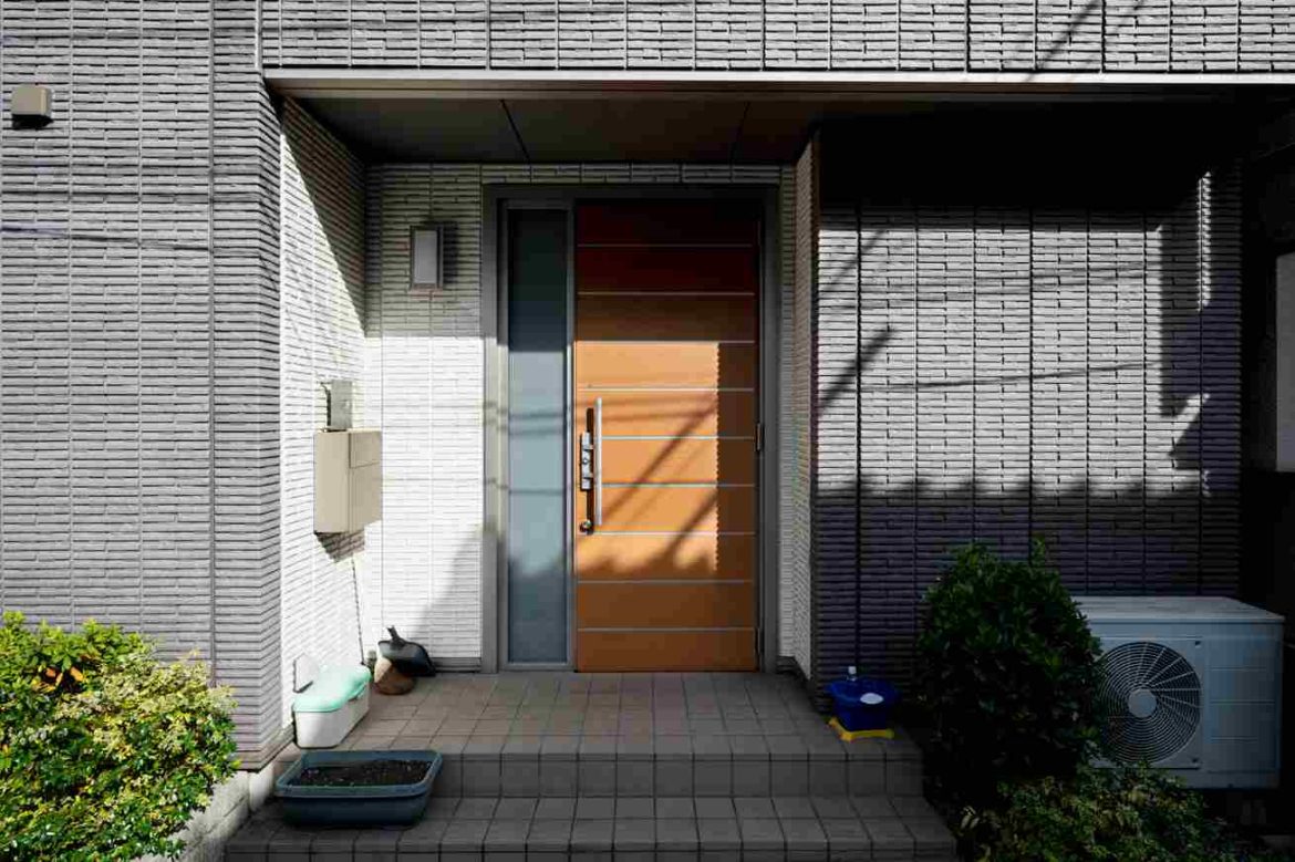 Entrée principale d'une maison moderne avec une porte d'entrée menuiserie pvc vitrée moderne de couleur bois et un panneau latéral vitré, encadrée par des murs en briques grises texturées.